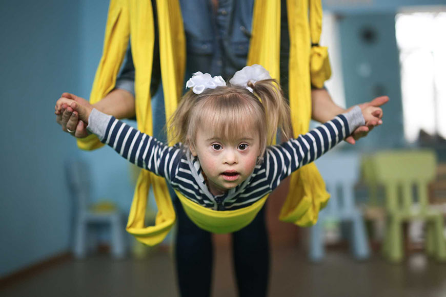Photo of a little girl in a therapy swing with therapist holding her steady