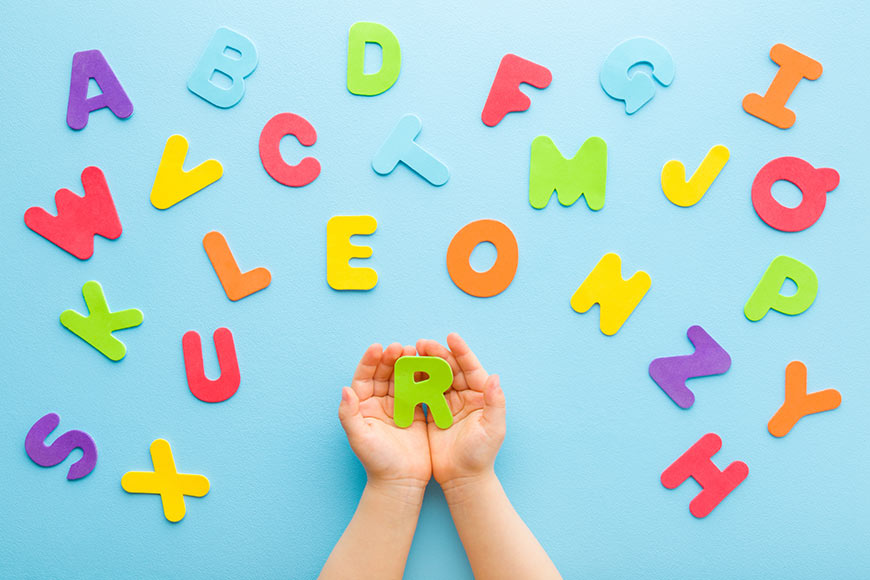 Photo of a child's hands holding paper letter R with other letters scattered n blue background
