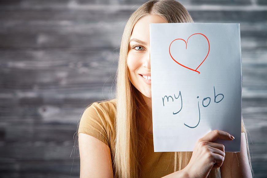 Photo of a woman holding up a sign that says love my job