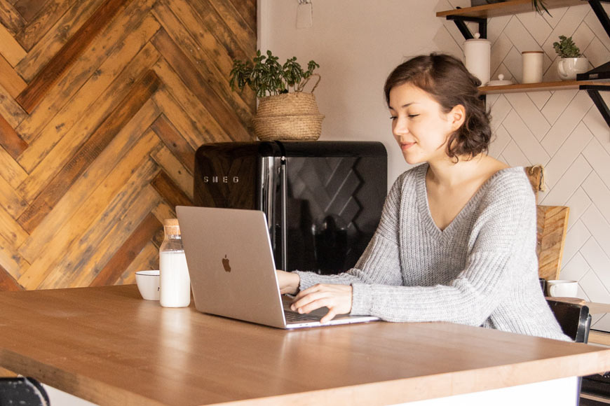 Positive young woman with laptop in modern kitchen